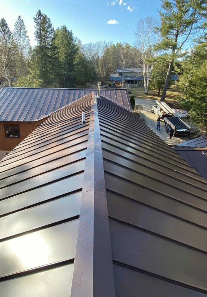 kki Brown standing-seam metal roof ridge overlooking wooded residential property.