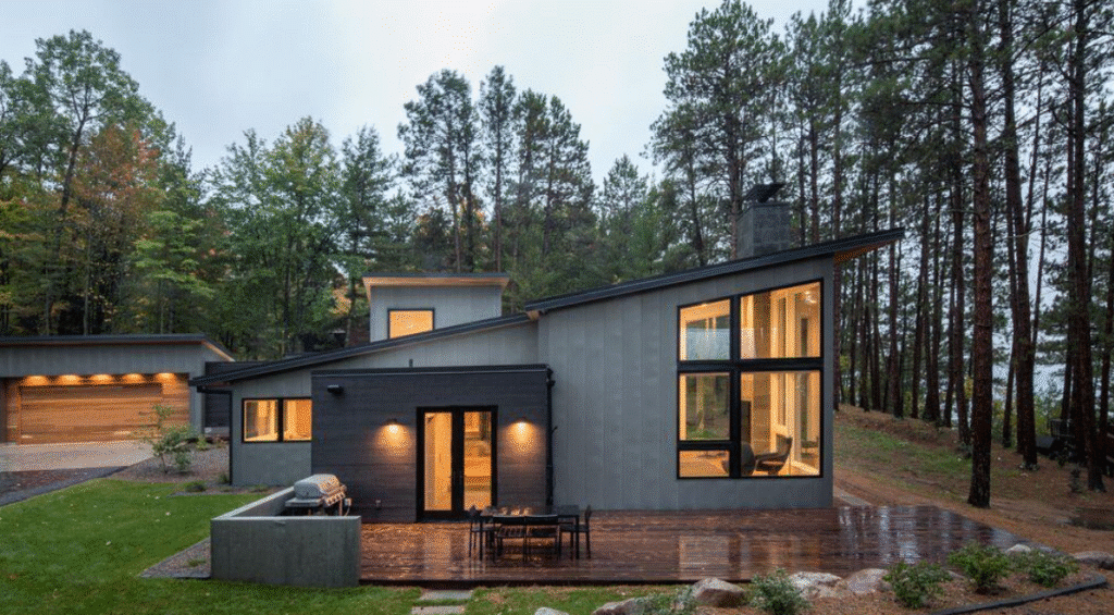n Contemporary gray metal-clad home with large windows set among pine trees.
