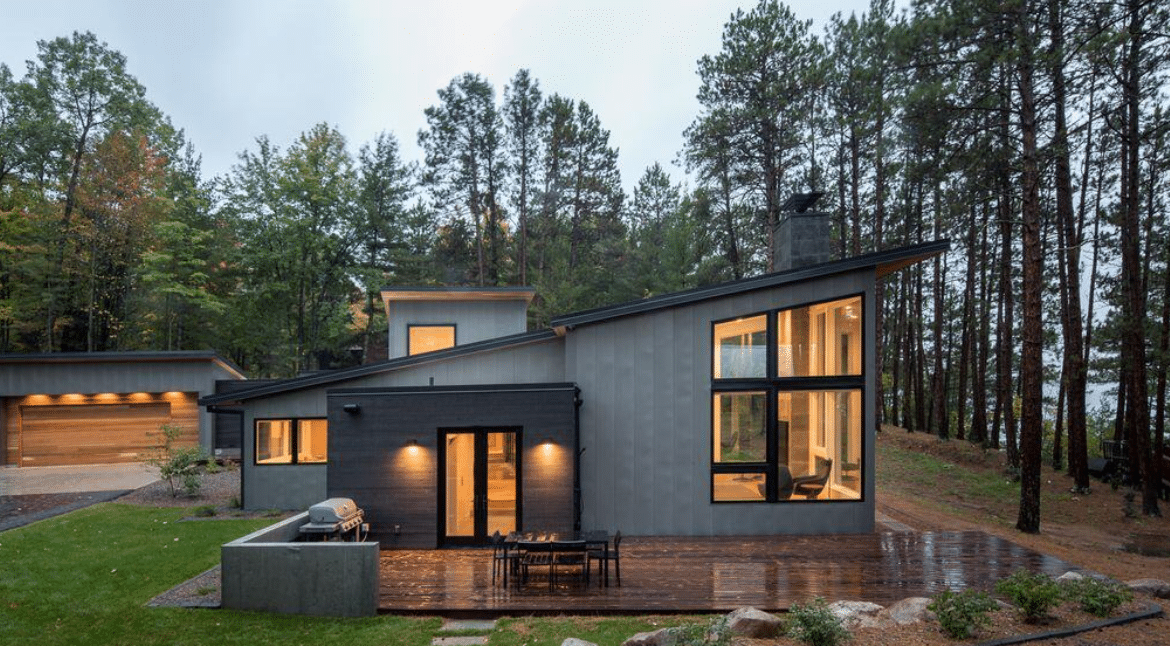 n Contemporary gray metal-clad home with large windows set among pine trees.