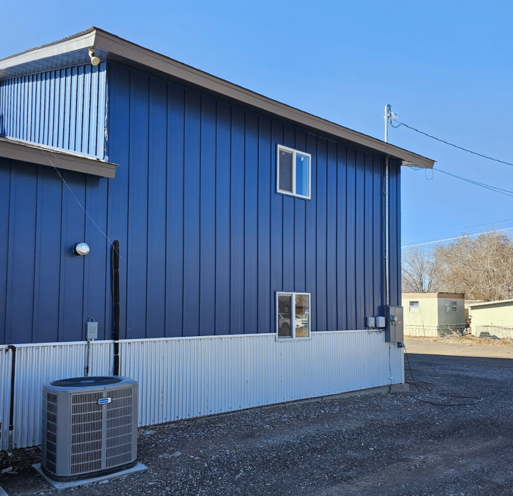 v Blue metal-sided building with white corrugated lower wall and outdoor AC unit.