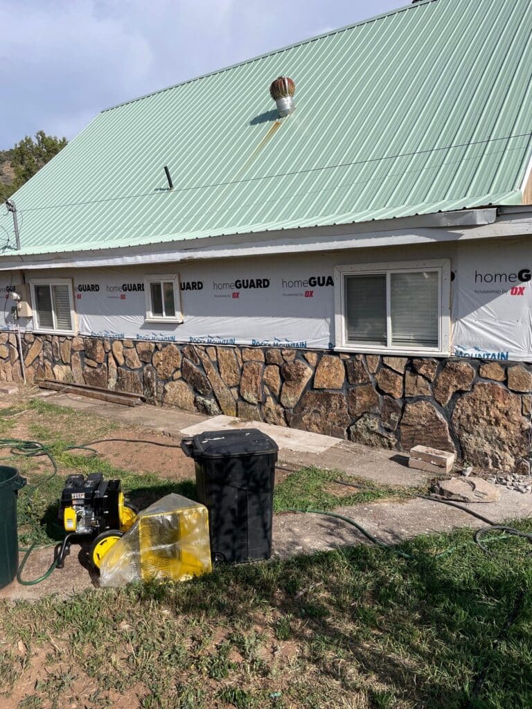 MzhkOGQ4YmUuanBn Green metal roof on a residential building with a stone exterior, visible roof vent, and construction materials in the foreground