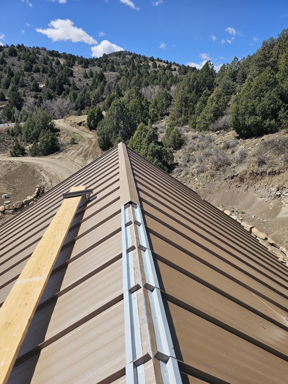 Standing-seam roof ridge installation Brown standing-seam metal roof with the ridge cap partially installed.