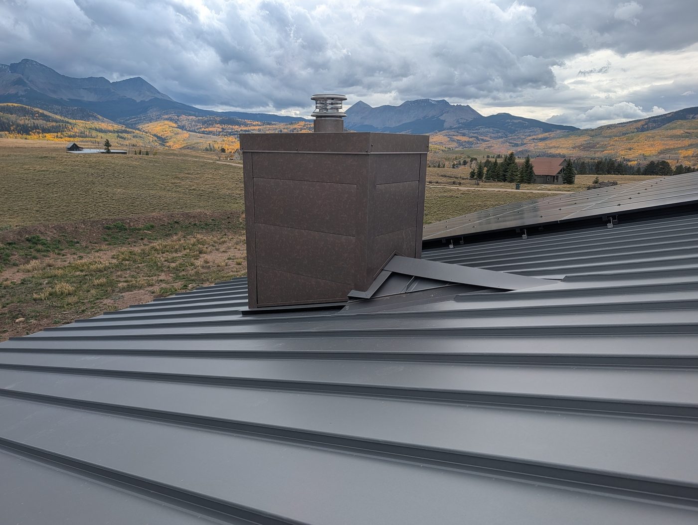 Metal-clad chimney chase on a gray standing seam roof with fall aspens near Telluride